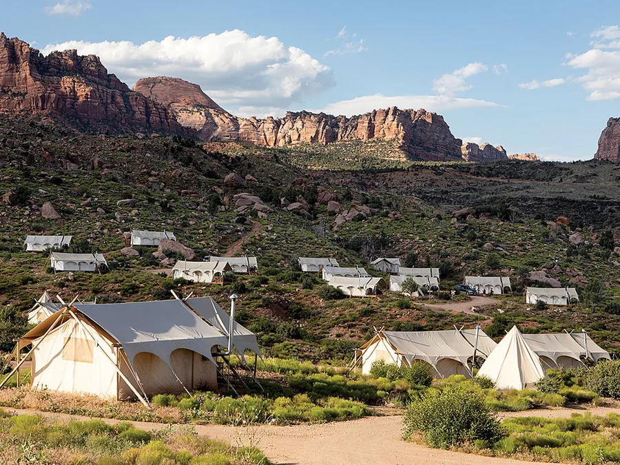 White safari tents scattered across red-rock desert scrub beneath sandstone cliffs.