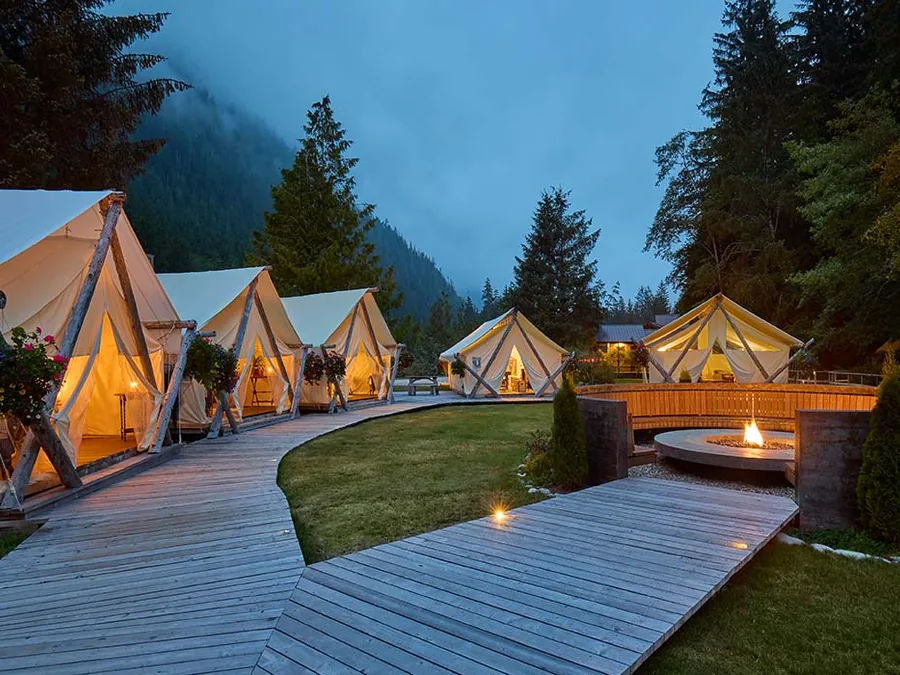 Peaked white tents around a boardwalk fire pit at dusk in the mountains.
